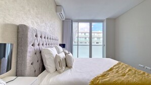 Une chambre d’hôtel moderne dotée d’un grand lit, d’un téléviseur à écran plat et offrant une vue sur un immeuble par la fenêtre.