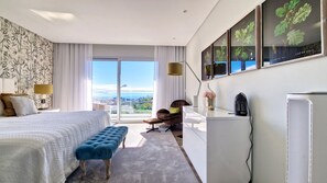 A modern hotel room with a large bed, a seating area, a desk, and a view of the city.