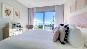 A modern bedroom with a large bed, a city view through floor-to-ceiling windows, a chaise lounge, and a dresser with decorative items. - 24, The Townhouse by Lovelystay (Funchal)