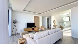 A modern living room with a large sofa, a flat-screen TV, and a wooden entertainment unit. - Ohana Ocean View by LovelyStay (Arco Da Calheta)
