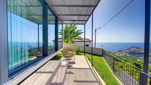 A balcony with a view of the sea, a glass wall, and a small garden area with chairs and a table. - Serenity Valley Escape by LovelyStay (Ribeira Brava)