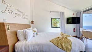 A hotel room with a large bed, a mounted TV, a window with a view of greenery, and a motivational quote on the wall. - Serenity Valley Escape by LovelyStay (Ribeira Brava)