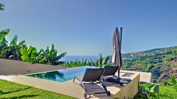 A pool with two lounge chairs and a table, surrounded by tropical plants, overlooking a coastal landscape. - Serenity Valley Escape by LovelyStay (Ribeira Brava)