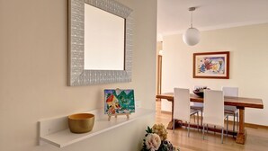 A dining area with a wooden table, white chairs, a hanging light fixture, and a framed painting on the wall. - Lucy Sweet Home by LovelyStay (Canico)