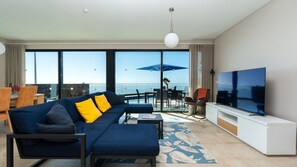 Un salón moderno con sofá, televisión y grandes ventanales con vistas al mar.