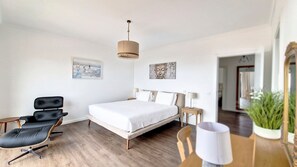A modern bedroom with a bed, a chair, a lamp, and artwork on the walls.