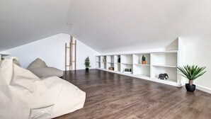 A spacious loft with a high ceiling, a built-in white shelving unit, a large bean bag, and a wooden ladder. - Costa Vista by LovelyStay (Funchal)