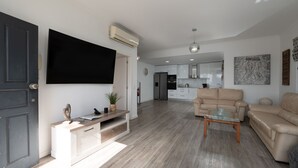 Un salon moderne avec un téléviseur à écran plat, un canapé, une table basse et une cuisine en arrière-plan.