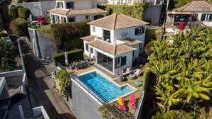 Une maison moderne à deux étages, dotée d’une piscine, entourée d’une végétation luxuriante et offrant une vue dégagée sur le quartier.
