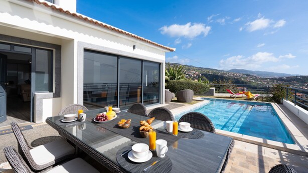 Une terrasse sur le toit avec une table à manger dressée pour le petit-déjeuner, une piscine et une vue panoramique sur la ville.