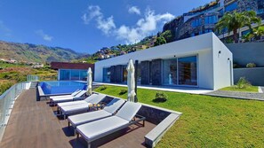 Um resort moderno com piscina, espreguiçadeiras e vista para as colinas ao redor.