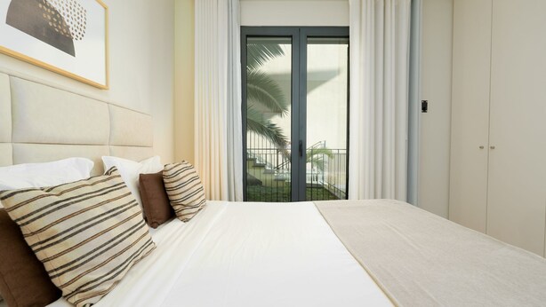 A hotel room with a bed, a framed picture, a balcony with a palm tree, and a sliding glass door.