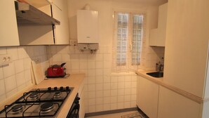 Une petite cuisine avec des meubles blancs, une cuisinière à gaz, un grille-pain rouge et une fenêtre ornée de rideaux à motifs.