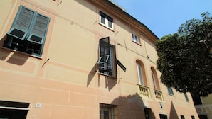 Un bâtiment à la façade beige, doté de nombreuses fenêtres avec volets et d’une porte verte.