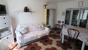 Un salon chaleureux avec un canapé, une table à manger et des chaises, un téléviseur posé sur un meuble et un sol à motifs.