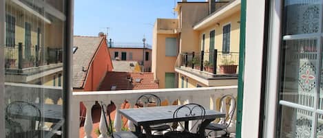 A balcony with a table and chairs, overlooking a row of buildings with red-tiled roofs and balconies.