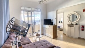 Een moderne hotelkamer met een groot raam, een flatscreen televisie, een bank, een eettafel en een badkamer met spiegel en kast.