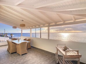 A spacious balcony with a view of the ocean, wicker furniture, and a wooden cart. - Naya Beach House by LovelyStay (Paúl do Mar)