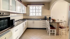 Een kleine keuken met witte kastjes, een ingebouwde oven, een koffiezetapparaat en een eethoek met een tafel en stoelen.