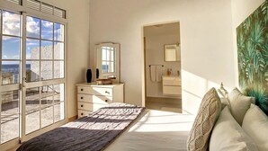 Een slaapkamer met een bed, een dressoir, een spiegel en uitzicht door een raam.