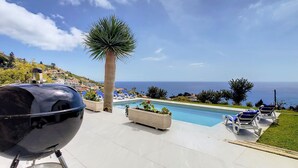 Blick auf einen Pool mit Grill, Liegestühlen und Meerblick.
