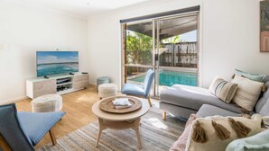 En stue med fjernsyn, sofa og udsigt til en pool gennem store skydedøre.