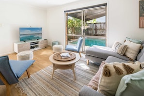 A living room with a TV, sofa, and a view of a pool through large sliding doors.