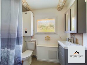 A bathroom with a toilet, a bathtub, and a window with a view of trees. - Gîte de la Draillette (Noves)