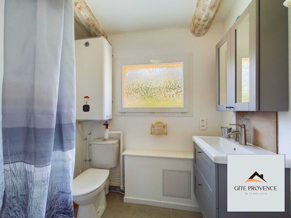 A bathroom with a toilet, a bathtub, and a window with a view of trees. - Gîte de la Draillette (Noves)