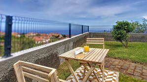 Une table, une chaise et un banc sont disposés à l’extérieur, offrant une vue panoramique sur un paysage agrémenté d’une clôture et de verdure.