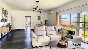 Un salon spacieux avec une grande fenêtre, un canapé, une table basse et un coin repas à l’arrière-plan.