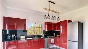 Une cuisine moderne avec des meubles de rangement rouges, un réfrigérateur en acier inoxydable et une fenêtre qui laisse entrer la lumière naturelle.