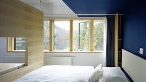 Une chambre à coucher avec un lit, une fenêtre avec des rideaux et une vue sur les arbres.
