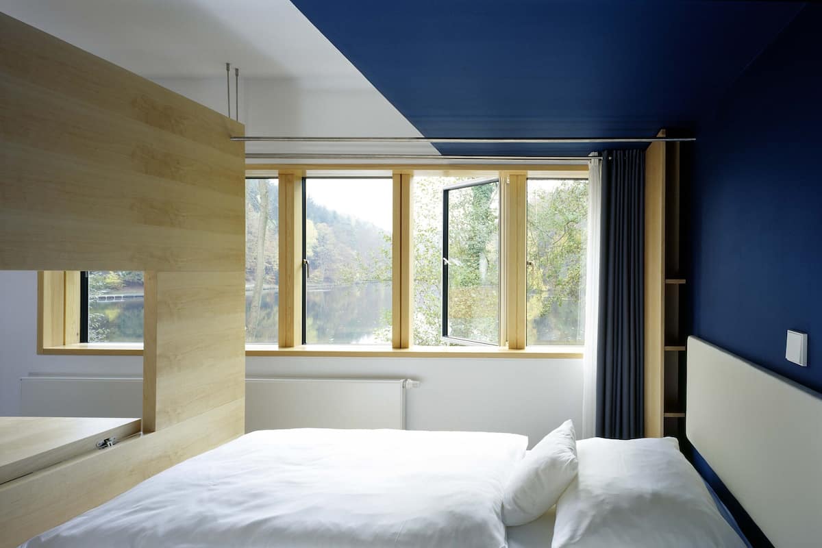 A bedroom with a bed, a window with curtains, and a view of trees.