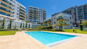 A modern apartment complex with a central swimming pool, multiple balconies, and a well-maintained garden.