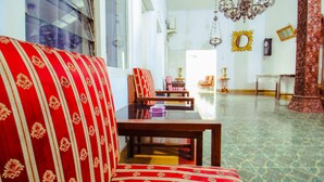 A room with a red patterned sofa, a wooden table, and a chandelier. - Prayogo Style Inn Prawirotaman (Yogyakarta)