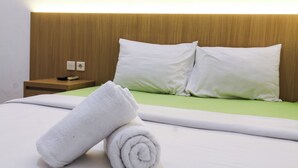 A neatly made bed with white linens and pillows, a rolled white towel, and a wooden nightstand with a remote control. - Prayogo Style Inn Prawirotaman (Yogyakarta)