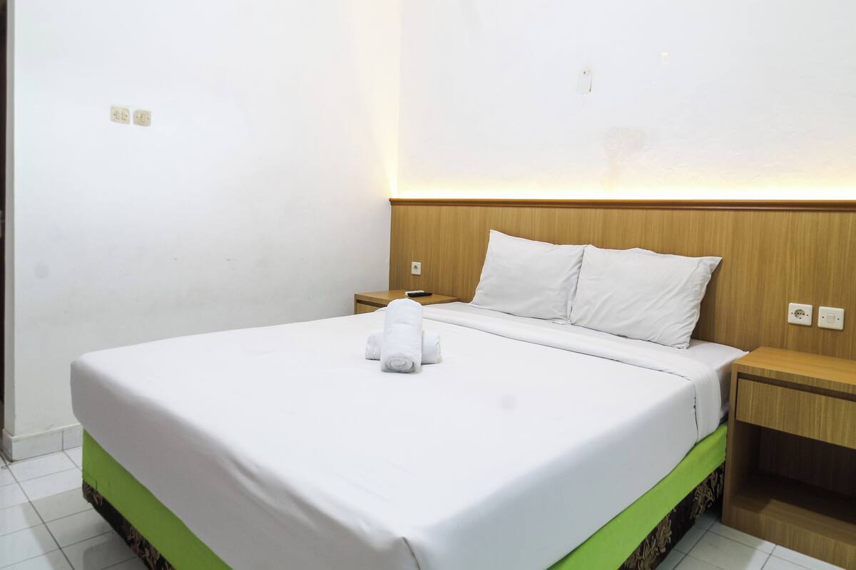 Una habitación de hotel con una cama bien hecha, un cabecero de madera y una mesita de noche con una lámpara.