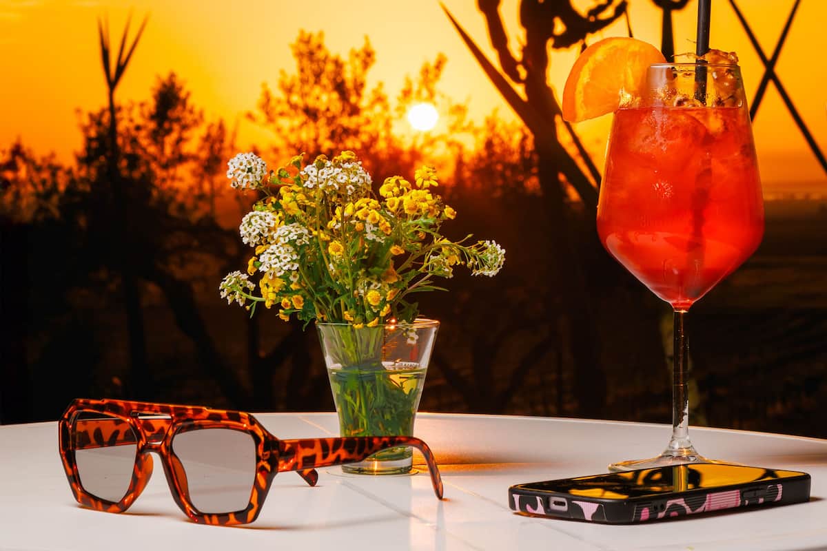 A table with a drink, a pair of glasses, and a phone.