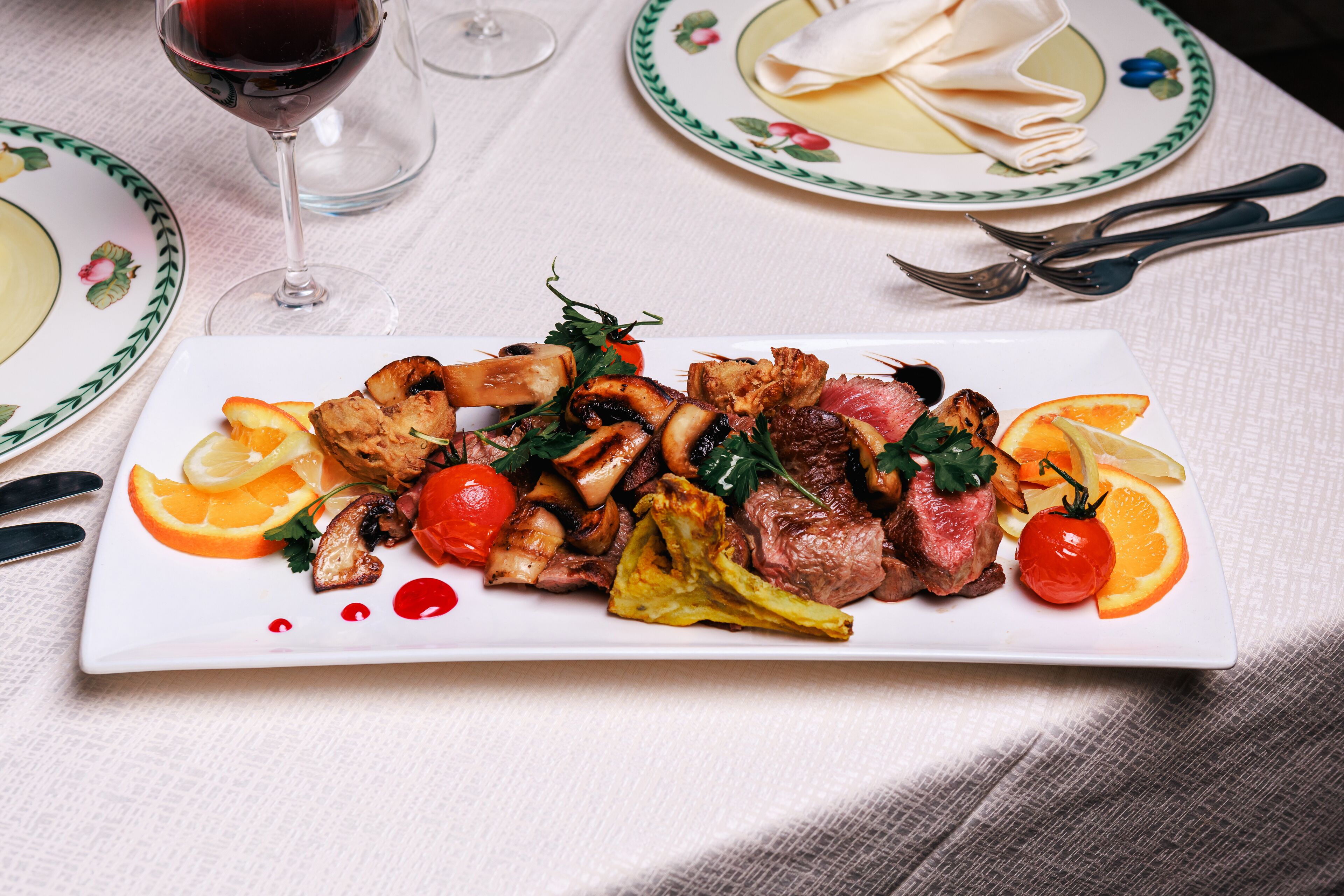 A plated meal with steak, mushrooms, and vegetables, accompanied by a glass of red wine.