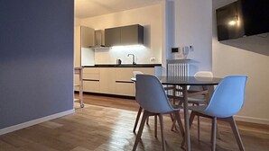 A modern kitchen with a dining area, featuring a table with chairs, a TV mounted on the wall, and a hanging light fixture. - Cozy apartment near the center, excellent for families (Bardolino)