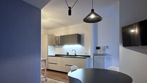 A modern kitchen with a dining area, featuring a round table and chairs, a pendant light, and a flat-screen TV mounted on the wall. - Cozy apartment near the center, excellent for families (Bardolino)