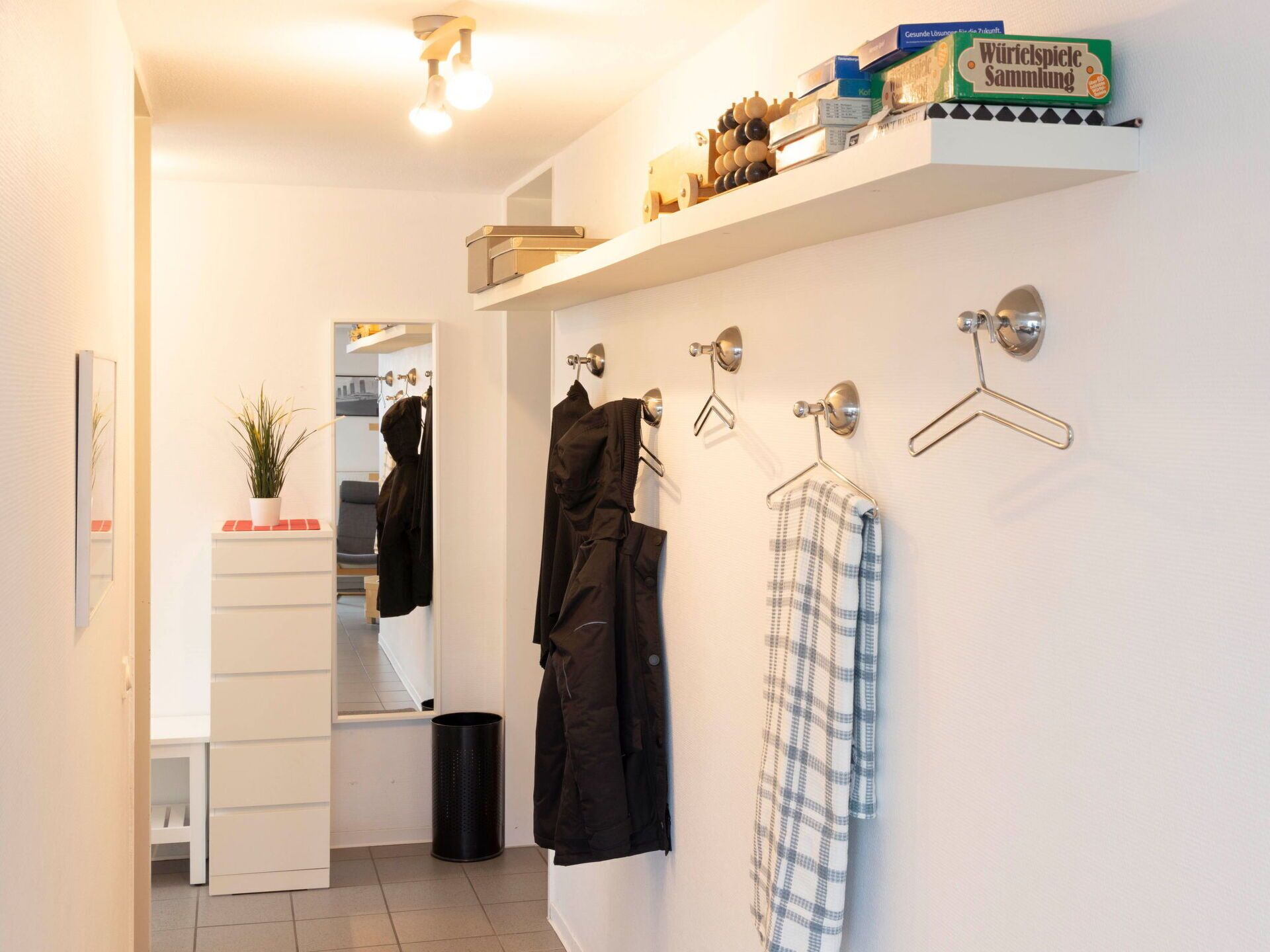 A modern bathroom with a white sink, mirror, and towel rack. There is a shelf with toiletries and a small potted plant.