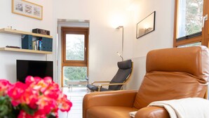 A modern living room with a leather armchair, a flat-screen TV, a bookshelf, and a dining table with fruit. - Beautiful apartment for 4 guests with WIFI, TV and balcony (Greifswald)