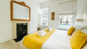 A hotel room with a large bed, a fireplace, and a view of the city through the windows. - Argyle St Apartments  (Bath)