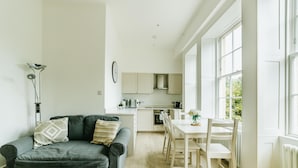 A modern kitchen with white cabinets and a dining area with a white table and chairs. - Argyle St Apartments  (Bath)