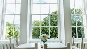 A room with a large window, a table with chairs, and a vase with flowers. - Argyle St Apartments  (Bath)