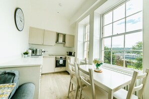 A kitchen with a view of a green landscape, a dining table with chairs, and a clock on the wall. - Argyle St Apartments  (Bath)