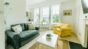 A modern living room with a grey sofa, a yellow armchair, and a white coffee table with a plant. - Argyle St Apartments  (Bath)
