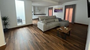 A modern living room with a large L-shaped sofa, a wooden coffee table, and a view of the kitchen through an open door. - El Balcón          . (Algodonales)